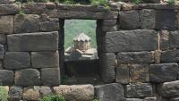 The view of a building through a window in a stone wall.